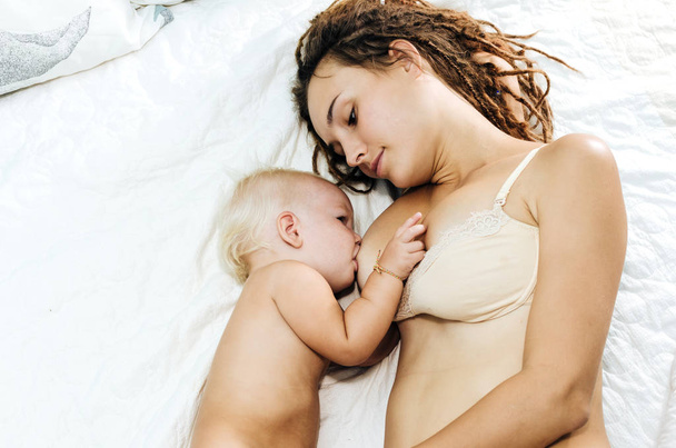Woman is breastfeeding her child. Mum and daughter lie on the bed. - Foto, Imagem