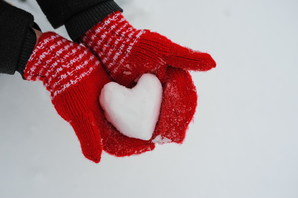 γυναίκα με τα κόκκινα γάντια κρατώντας ένα χιονισμένο καρδιά - Φωτογραφία, εικόνα