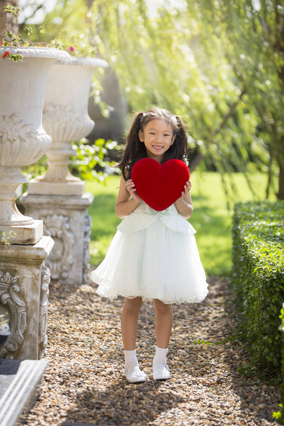 Kırmızı kalp yastık, holding beyaz elbiseli küçük kız Sevgililer  - Fotoğraf, Görsel