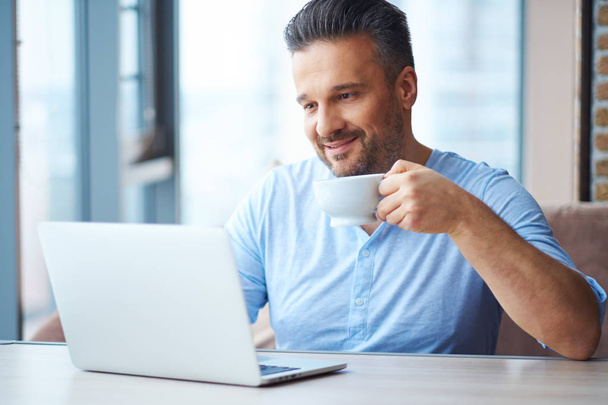 Schöner Mann mit Tasse Kaffee mit Laptop zu Hause - Foto, Bild