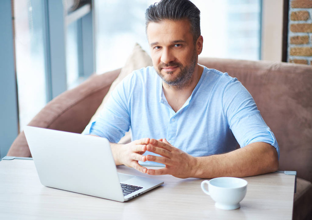 Handsome man with cup of coffee using laptop at home - Foto, immagini