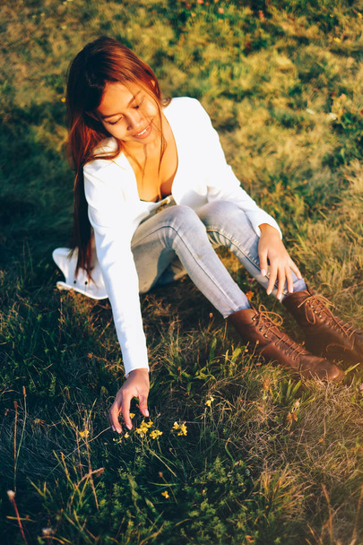 花と遊んで芝生の上に座っている美しい少女 - 写真・画像