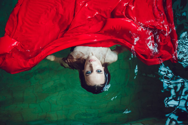Fashion brunette woman with beautiful professional make up floating in a pool of red cloth. - Fotoğraf, Görsel