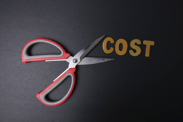 Pari sakset leikkaa liiketoiminnan kustannuksella sana COST säästää kustannuksia. Liiketoimintakonsepti ja heikko valo
. - Valokuva, kuva