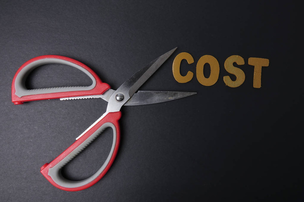 Nůžkami zastřihne obchodních výdajů slovo náklady pro úsporu nákladů. Obchodní koncept a nízké světlo. - Fotografie, Obrázek