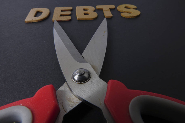 Schere und Schuldenwort auf schwarzem Hintergrund. Geschäftskonzept - Foto, Bild