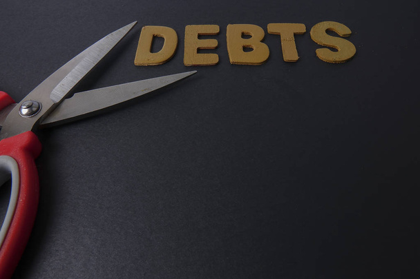 Sakset ja sana DEBTS mustalla taustalla. Liiketoiminta
 - Valokuva, kuva