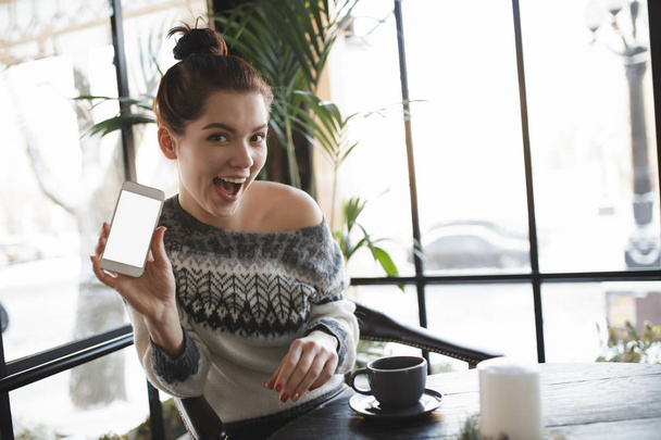 Woman teasing showing empty white screen of smartphone in a cafe - Photo, Image