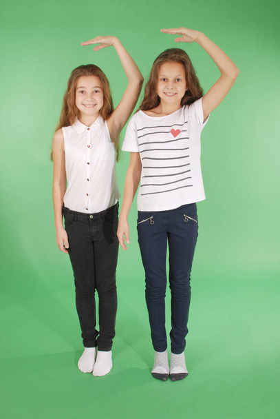 Dos niñas de la escuela toman las manos por encima de la cabeza y miden su crecimiento
 - Foto, Imagen