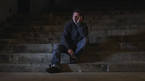 4k-Video seitliches Schwenken 24 fps junger verzweifelter verschwendeter Mann in Kapuze, der unter Stress und Traurigkeit leidet und nachts elend auf städtischen Straßentreppen sitzt, traurig und besorgt im Suchtkonzept - Filmmaterial, Video
