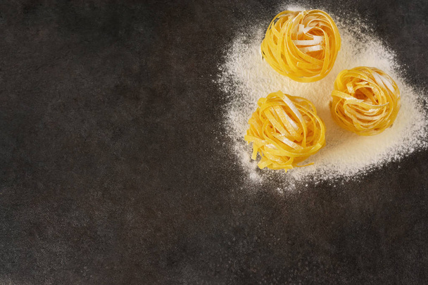 Raw tagliatelle pasta with flour on a black background - 写真・画像