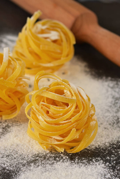 Raw tagliatelle pasta with flour on a black background - 写真・画像