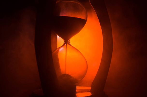 Концепция времени Силуэт песочных часов и дыма на темном фоне с горячим желтым оранжево-синим холодным задним освещением, или символы времени с копировальным пространством, песочными стеклами или песчаными часами
 - Фото, изображение