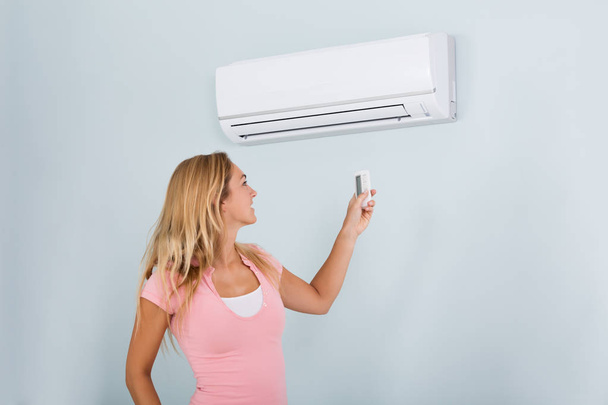 Woman Operating Air Conditioner  - Foto, Bild
