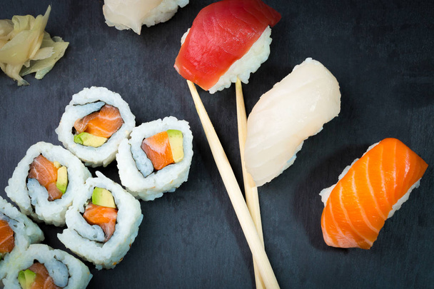 Sushi y Sashimi ruedan sobre una pizarra de piedra negra. Set de Sushi recién hecho con salmón, gambas, wasabi y jengibre. Cocina tradicional japonesa
 - Foto, Imagen