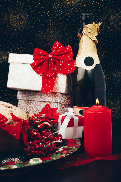 Noël ou Nouvel An. Champagne dans des verres avec des bougies, panettone et cadeau avec arc en satin rouge
. - Photo, image