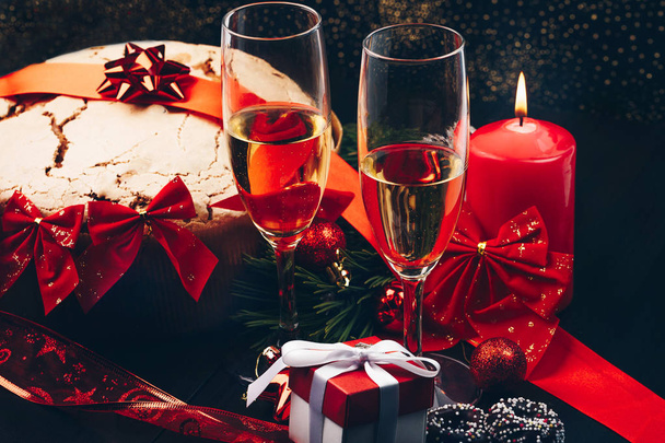 Vánoce nebo nový rok. Champagne v brýlích se svíčkami, panettone a dárek s červenou saténovou mašlí. Kopírování prostor. Slavnostní koncepce - Fotografie, Obrázek