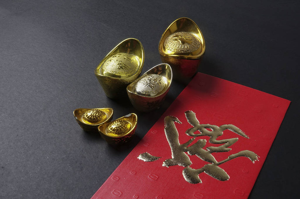 Gold ingots and red money packet for Chinese New Year festive on black background. Chinese character means luck,wealth and prosperity. Low light - Photo, Image