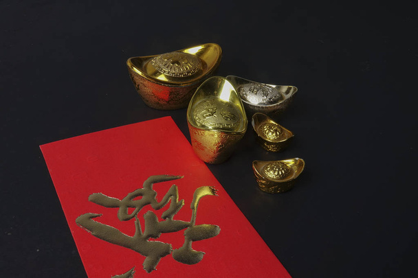 Gold ingots and red money packet for Chinese New Year festive on black background. Chinese character means luck,wealth and prosperity. Low light - Valokuva, kuva