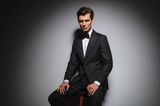 successful elegant man in tuxedo and bowtie sitting on stool  - Fotografie, Obrázek