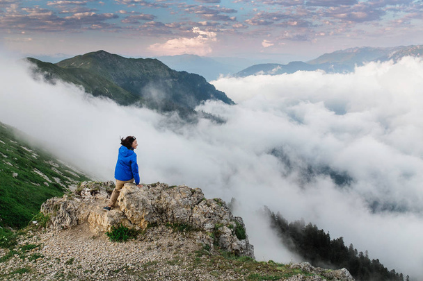 Femme touriste assis sur un sommet de montagne et bénéficie d'une vue imprenable sur la vallée de montagne brumeuse
. - Photo, image