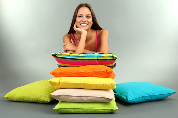 beautiful young girl with pillows on grey background - Foto, afbeelding