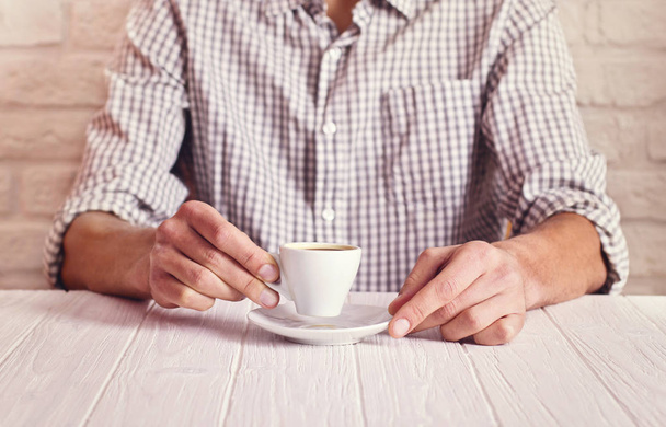 Coffee break. Man sitting on the white table with cup of espresso in the checked shirt. White bricks wall background - Foto, Imagen