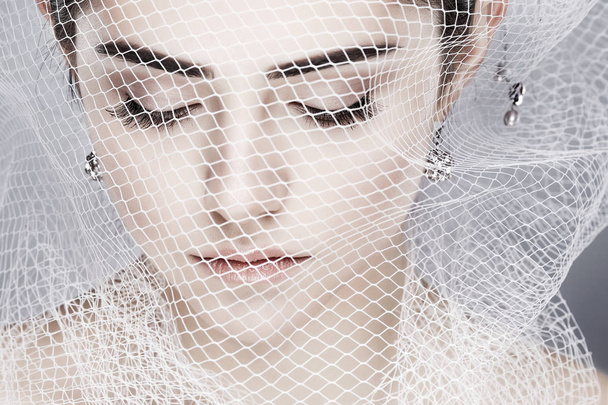 A beautiful girl is in a white veil, isolated on a light - grey background, emotions, cosmetics - Foto, imagen