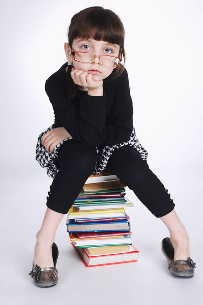 girl makes homework sitting on stack books - Foto, afbeelding