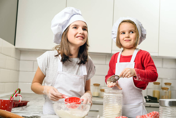 Sisters making dough in white kitchen - Foto, afbeelding