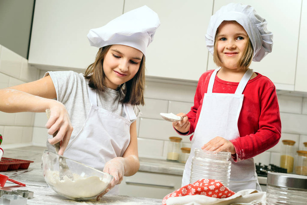 Sisters making dough in white kitchen - Foto, afbeelding