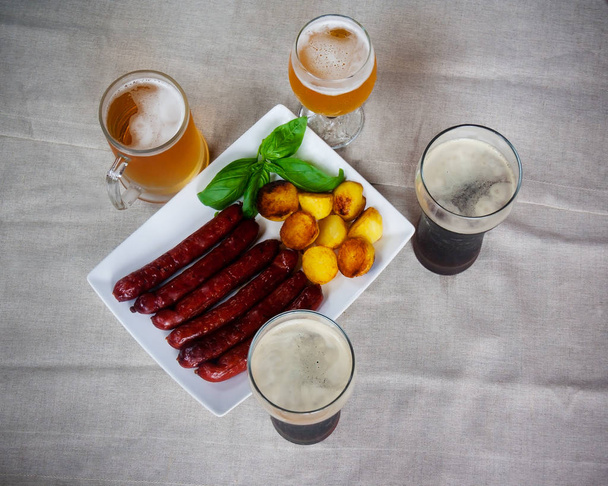 Pork sausages on white plate , glasses of beer, roasted potatoes - Photo, image