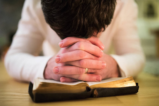 Unrecognizable man praying, kneeling on the floor, hands on Bibl - Фото, изображение