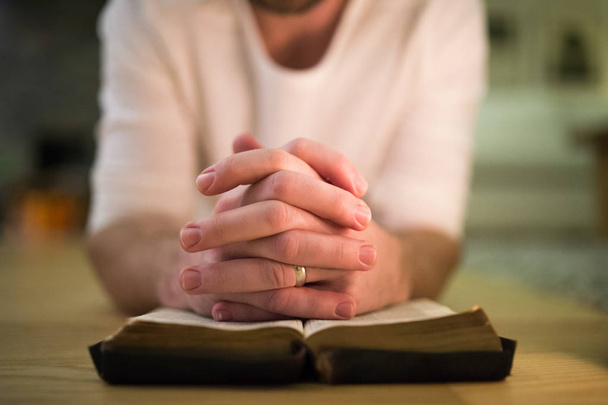 Tunnistamaton mies rukoilee, polvistuu lattialle, kädet Bibl: llä
 - Valokuva, kuva