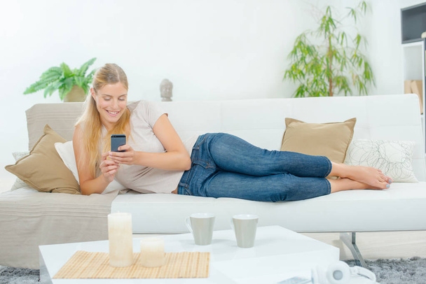 Lady layed on couch, looking at cellphone - Foto, Bild