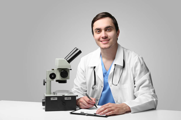Young doctor working with microscope at table on light background - Foto, afbeelding