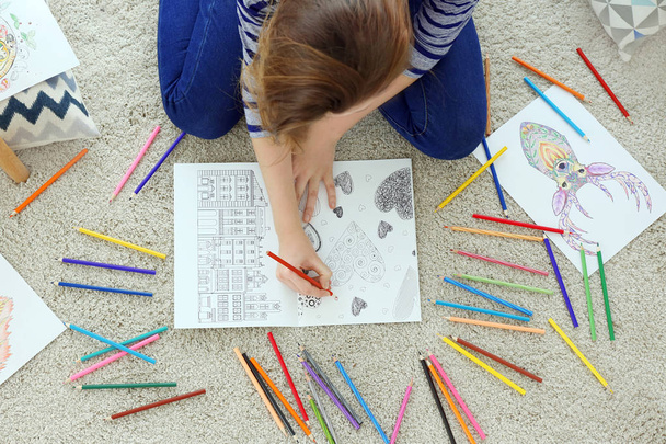 Young woman sitting on floor with coloring pictures for adults - Foto, Bild
