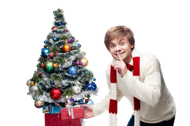 Young smiling man puts gift under christmas tree - Fotografie, Obrázek