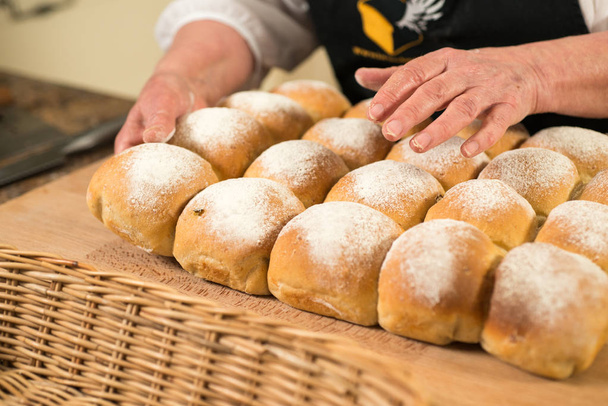 Baker's hands over a cluster of baked bread buns on a wooden countertop - Photo, Image