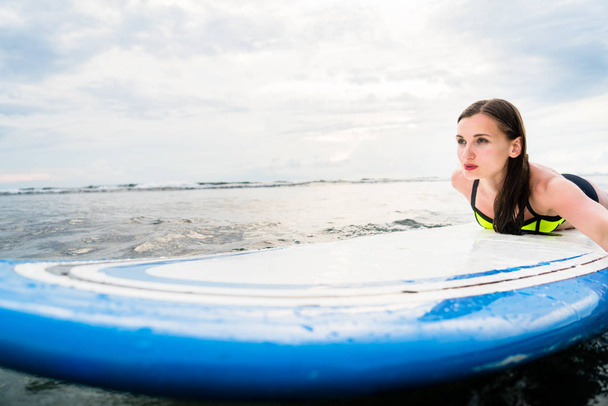 Tyttö surffaaja melontaa surffilaudalla avomerelle
 - Valokuva, kuva