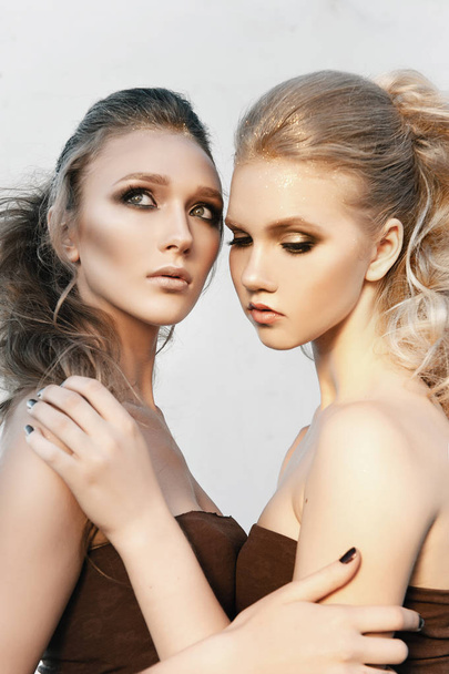 Glamour make-up twee vrouwen met lange haren stijl zittend op straat muur achtergrond in donker. Fashion kleur portret, geretoucheerde foto - Foto, afbeelding