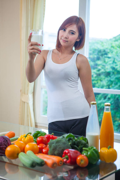 Young asian woman drinking milk in kitchen - Foto, afbeelding
