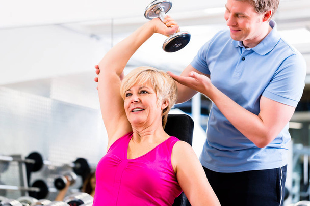 Senior vrouw in sport uitoefenen in de fitnessruimte met trainer - Foto, afbeelding