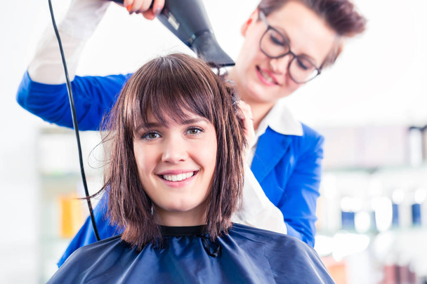 Перукар дує сухе волосся жінки в магазині
 - Фото, зображення