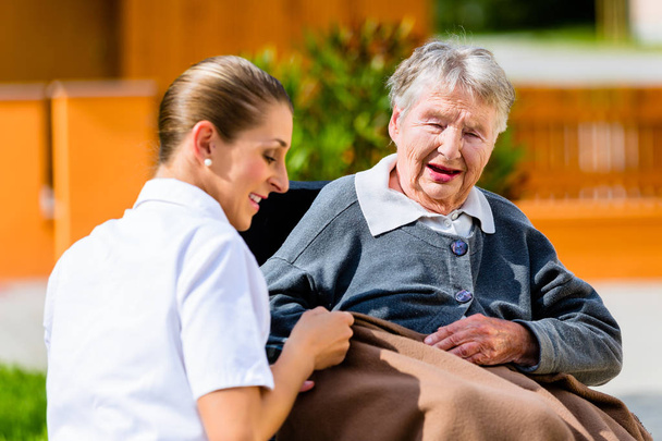 Sairaanhoitaja kädestä vanhempi nainen pyörätuolissa
 - Valokuva, kuva