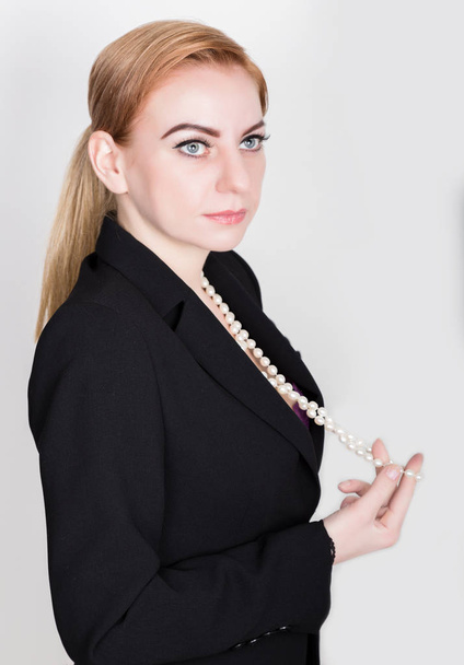 Mulher de negócios atraente e enérgica em um terno no corpo nu sorrindo, segurando pérolas
 - Foto, Imagem