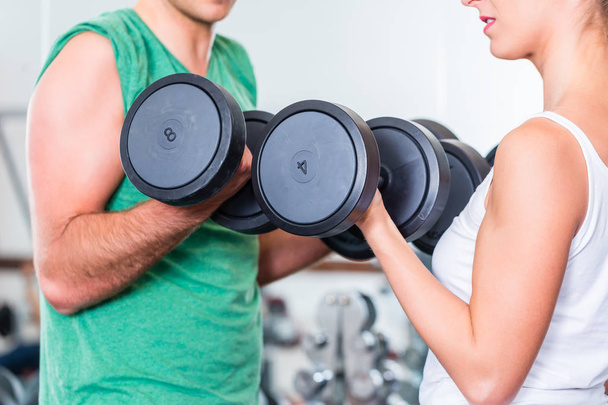 young couple in gym lifting dumbbells - 写真・画像