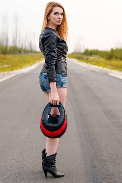 beautiful woman biker standing on the road with a motorcycle helmet in hand - 写真・画像