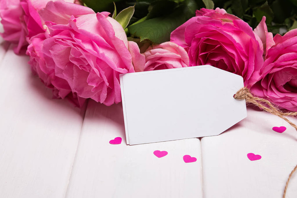 Beautiful pink roses and empty paper card on the white wooden ta - Fotografie, Obrázek