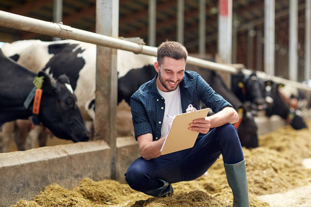 farmer with clipboard and cows in cowshed on farm - Foto, Bild